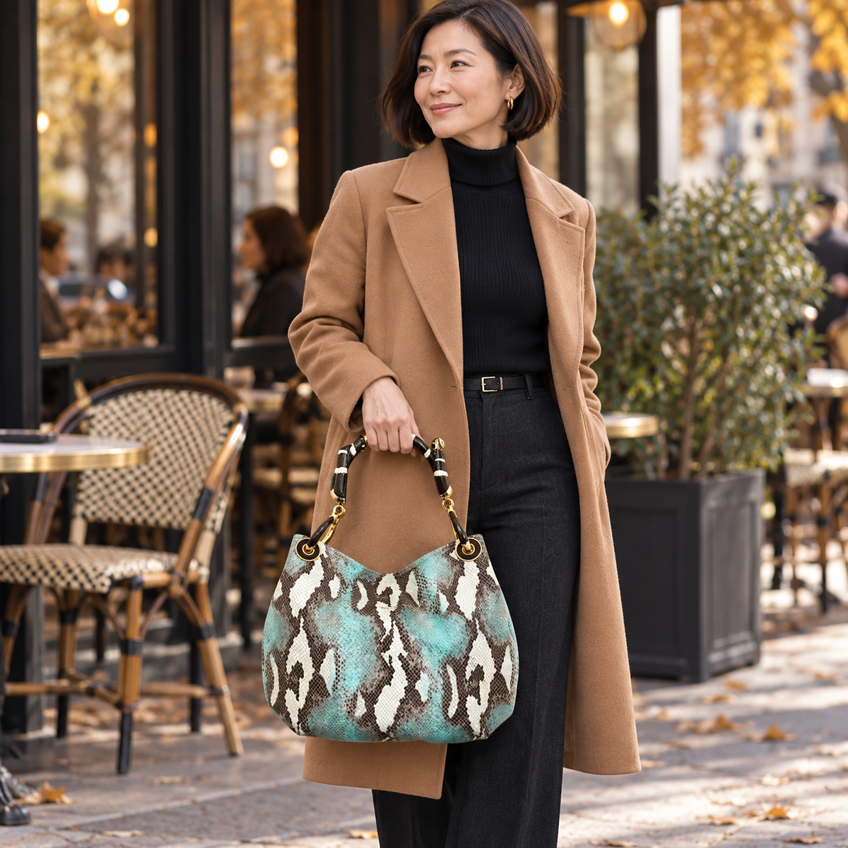 Woman carrying the INGA turquoise python-print leather medium handbag with black snake sculpture handle, styled for autumn.